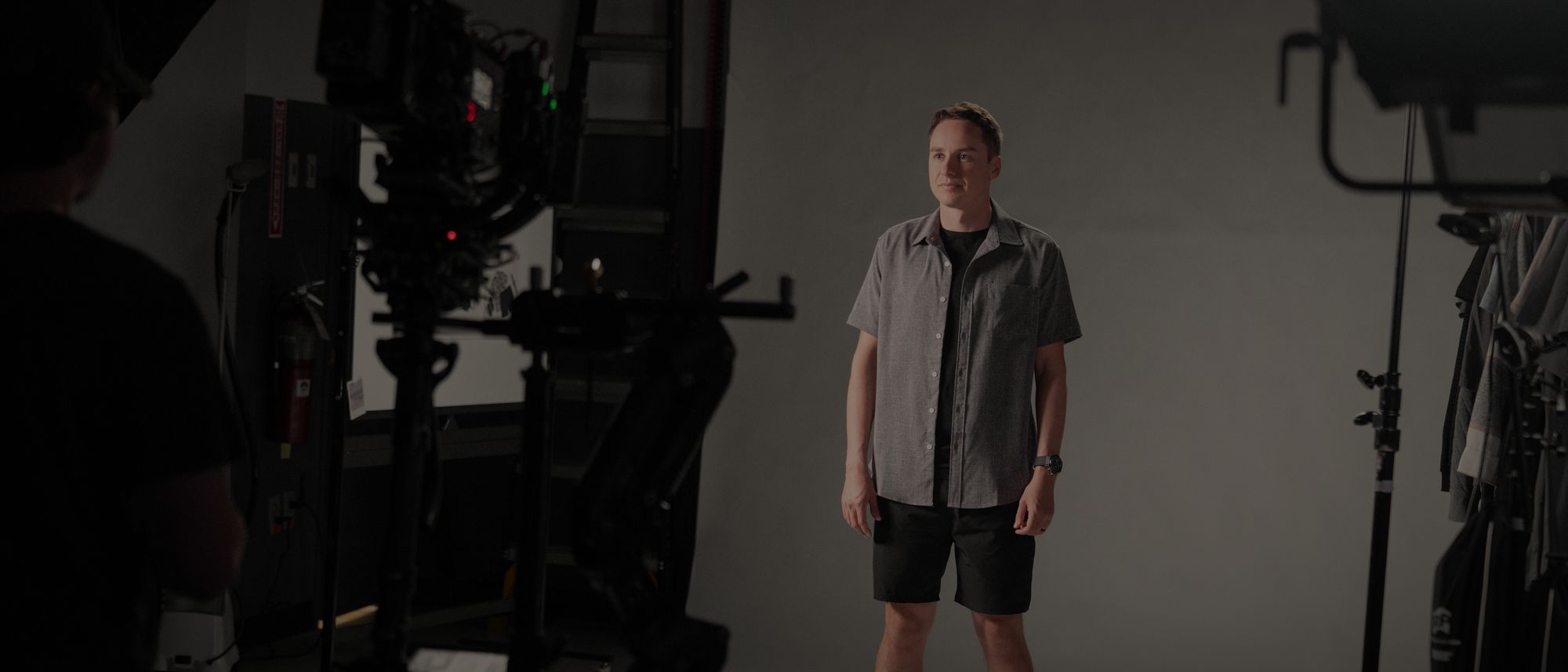 Christopher Bell stands on a white cyc in a grey shirt while a camera rig waits in the foreground