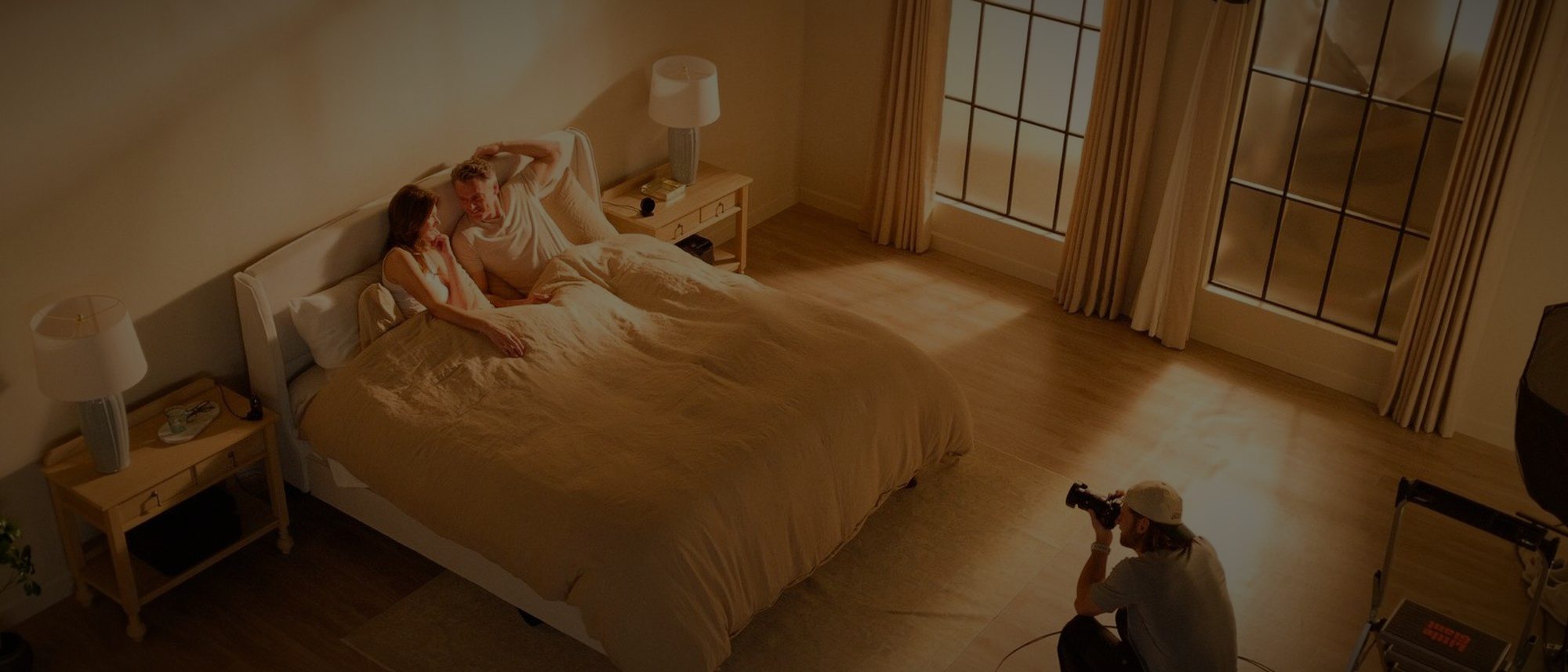 A dressed bedroom set lit for camera, with an operator working low to the floor.