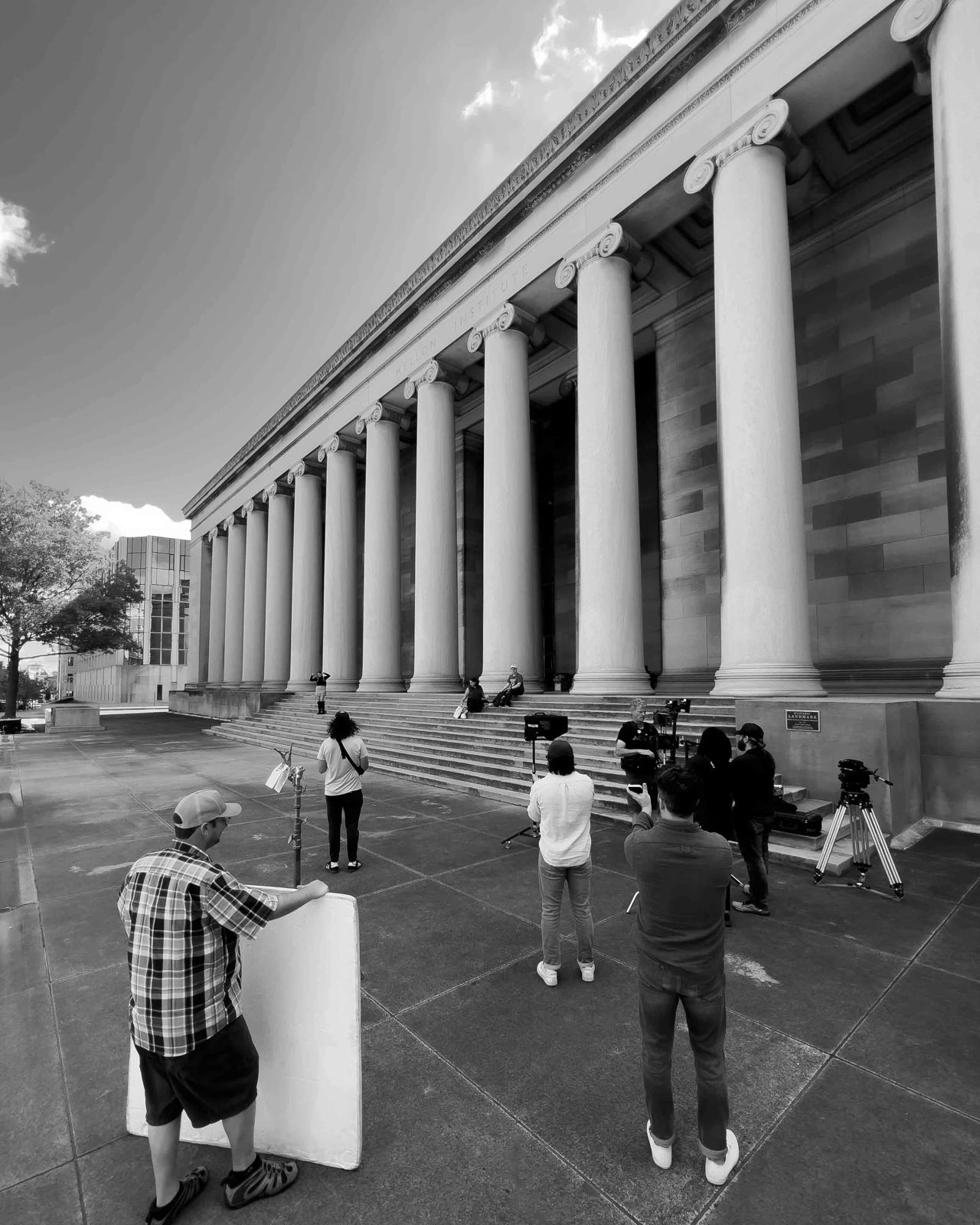 Black and white behind-the-scenes photo of the What If? crew filming on campus in front of a columned building