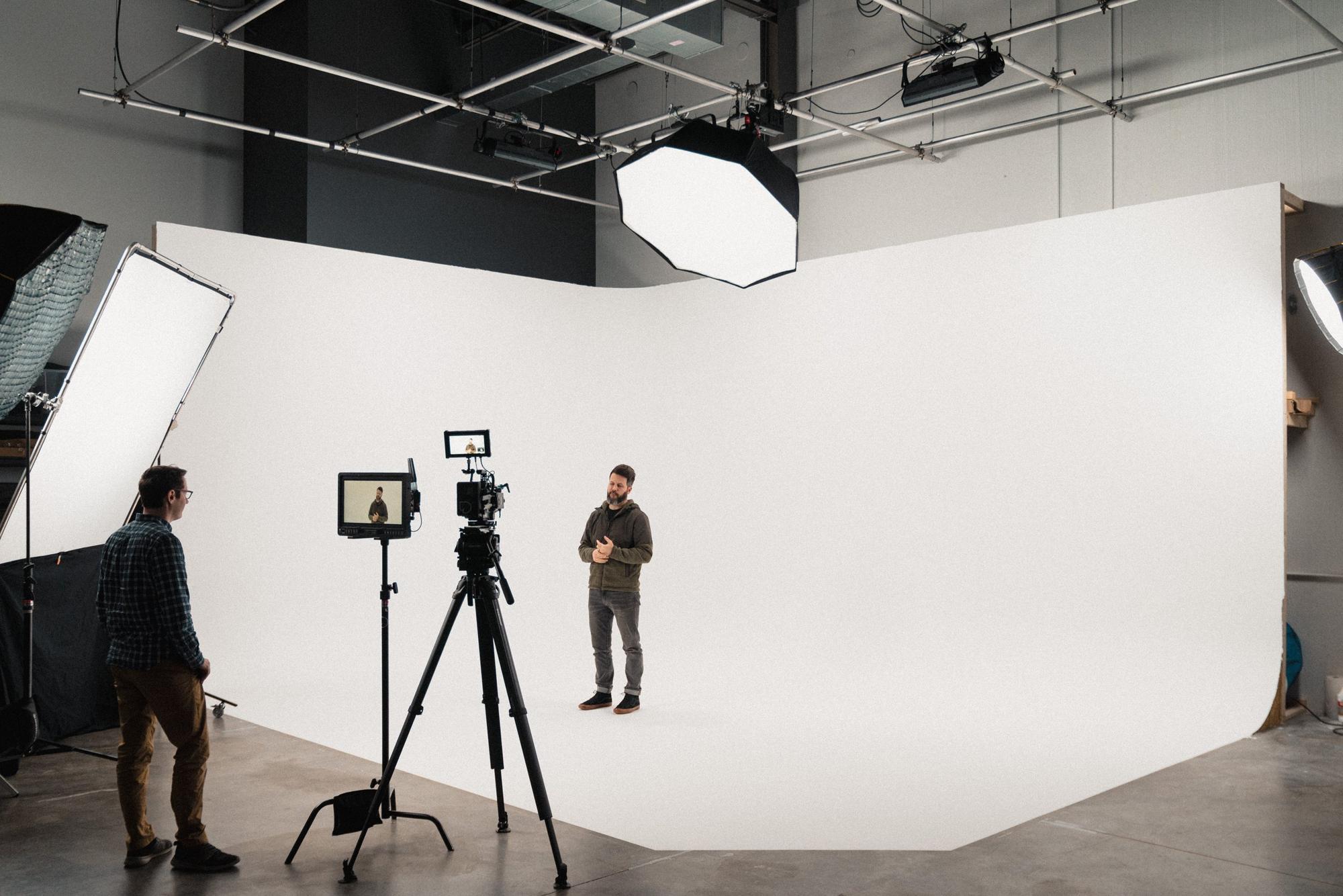 Crew filming a presenter against the white cyc, with a softbox and monitor on stands